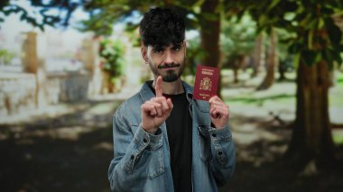 Parkta İspanyol pasaportu taşıyan, seyahat ve kimlik temalarını vurgulayan ve rahat bir şekilde ayakta duran bir adam..