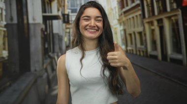 Genç İspanyol kadın gülümseyerek caddede yapıyı işaret ediyor; iyimserlik güven neşe enerjisi.