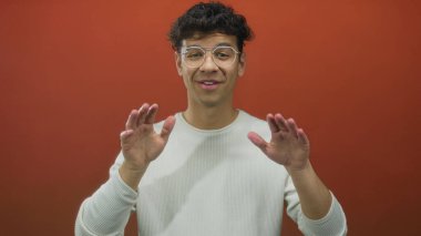 Genç İspanyol adam iki elini de kırmızı stüdyo duvarına dayayıp sakin bir duraksama için işaret veriyor..