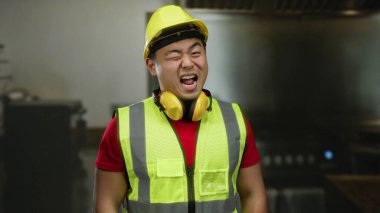İnşaat işçisi, güvenlik kaskı ve çelik yelek giyerek sanayi ortamında gülerek Asyalı erkek enerji ve profesyonelliğini vurgulayan koruyucu kulaklık takıyor..