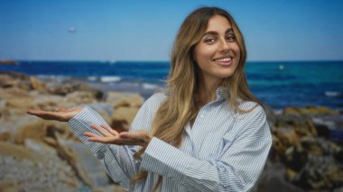 Gülümseyen genç sarışın kadın kayalık deniz kıyısında avuçlarını açık tutuyor; davetkar keşif huzur neşe özgürlüğü.