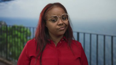 Kırmızı tişört giyen ve gözlüklü bir kadın manzaraya tepeden bakan balkon yapılmasını hoş karşılamıyor..