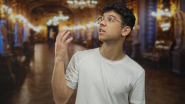 Adam avuç içi kaldırarak elini tutar ve süslü galeri binasındaki mermer heykele bakar; merak.