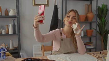 Bir çömlek atölyesinde selfie için akıllı telefon yetiştirirken kadın kilden kalbi tutuyor; yaratıcılık kendini ifade etme neşesi.