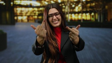 Açık havada gülümseyen İspanyol kadın gece aydınlanmış şehir caddesinde kaba bir jest yapıyor..