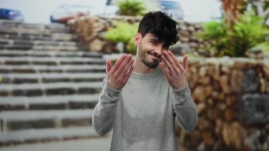 Genç adam şehir sokaklarında güven ve cazibeyle jestler yapıyor, taş basamaklar ve yeşilliklerle çevrili, anlamlı bir anı yakalıyor..