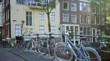 Bokeh efektli bulanık amfi kanal sahnesi, günışığı altındaki geleneksel Hollandalı evlerin odaksız arka planına karşı bisikletleri vurguluyor.