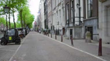 Ağaçların kaldırım taşı yolu kapladığı, bisikletleri park ettiği, hareketli ama sakin Avrupa kentsel ortamını vurgulayan Amsterdam Caddesi 'nin bulanık görüntüsü.