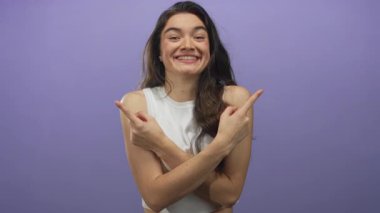 Genç kadın parmaklarını göstererek stüdyoda mor arka planda çıplak kollarını ve beyaz ekin üstünü gösteriyor; mutluluk..