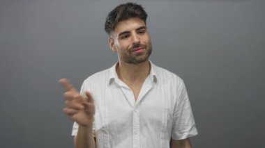Stüdyoda, gri arka planı ve beyaz gömleği olan, yüzü odaklanmış, özgüveni olan genç İspanyol bir adam var..