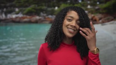 Kırmızı kollu uzun kollu Afro-Amerikalı kadın, turkuaz deniz kenarındaki yüzüyle dudaktan dudaklara kıvırcık saçlı, sessiz bir an..