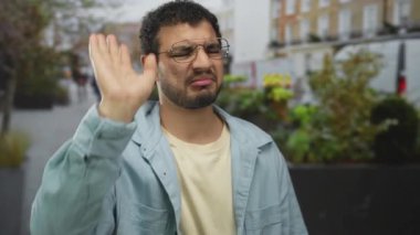 Açık mavi ceketli genç adam sokak manzarasını engelleyen dur jestinde el ele tutuşuyor; iğrenme reddedilme uyarısı.