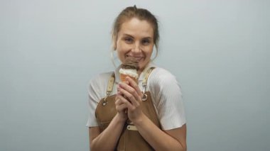 Önlüklü genç sarışın kadın izole edilmiş beyaz arka planda dondurma tutmayı seviyor, neşe ve memnuniyet saçıyor..