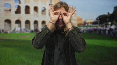 Sarışın adam geniş bir gülümseme içinde temiz gökyüzü altında antik kolezyum binasında el ele tutuşmuş, merak.