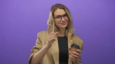 Mor arka planda kahve bardaklarıyla gülümseyen bir kadın, sarı saçlı ve bej ceketli, kendine güvenen, parmak işareti yapan bir kadın..