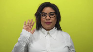 Beyaz gömlekli, parlak sarı arka planda sallanan bir kadın, dostça bir tavır sergiliyor, temiz gözlüklü, neşeli, yaklaşılabilir bir etkileşim öneriyor..