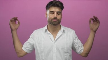 Gözleri kapalı İspanyol genç adam pembe stüdyoda elleri ile işaret, dinginlik, farkındalık meditasyonu gösteriyor.