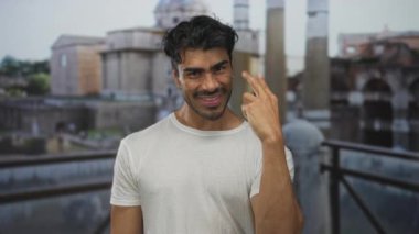 Beyaz gömlekli İspanyol adam güneşli gökyüzünün altındaki antik Roma harabelerinde üç parmağını gösteriyor..