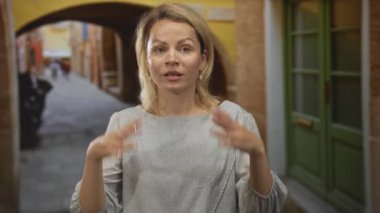 Elleri çıplak bir kadın, tarihi binaların ortasında güneşli bir kaldırım taşı caddesinde omuz silkme jesti ile açık bir sorgulama;.