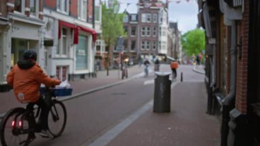 Bisikletçiler bulanık bir caddede gezerler, hareket halindeki insanlarla şehir yaşamını ve yumuşak odak noktasındaki canlı mimariyi yakalarlar..