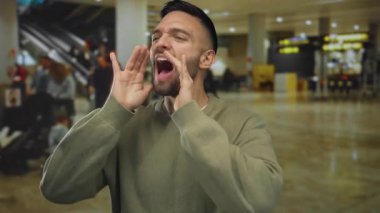 Havaalanı terminalinde bağıran İspanyol adam hareketli gezginler ve ışıklı işaretlerle dolu, canlı bir atmosfer ve acil seyahat seti yakalıyor..