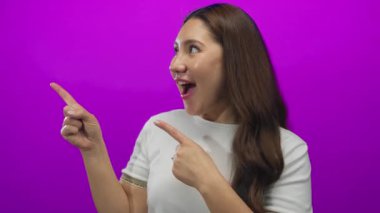 Stüdyo sahnesinde gülümseyen ve her iki işaret parmağını da sola gösteren İspanyol genç kadın..