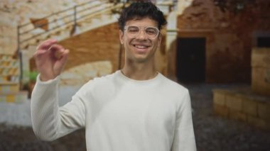 Gün ışığı altında güneşli, eski bir taş binanın önünde ok işareti yapmak için elini kaldıran adam onaylandı..