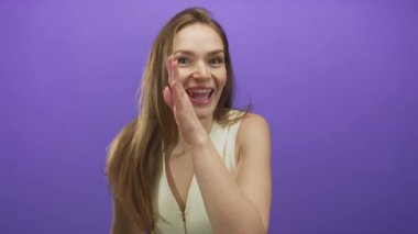 Kafkasyalı genç bir kadın el ele bir fısıltı jest yapıyor ve mor stüdyoda gülümsüyor..