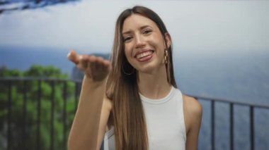 Genç Hispanik kadın, güneşli deniz kıyısında uzanmış elleriyle öpücük üflüyor altın saatte; sıcaklık.