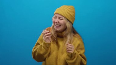 Kurabiyeli, sarı kazaklı, mavi arka planda şapkalı neşeli ve mutlu bir kadın..