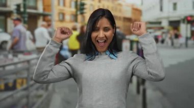 Kalabalık bir sokakta kolları havada enerjik bir şekilde kutlama yapan bir kadın, şehir bölgesinde neşe ve heyecan yakalıyor..