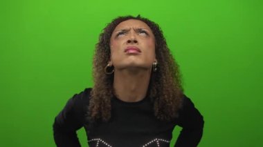 Transseksüel İspanyol kadın iki elini de yeşil stüdyo ortamında bükülmüş bir ifadeyle yukarı bakarken başını tutuyor..