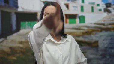 Güneşli bir sahil manzarasında küçümseyen bir ifadeyle, arka planda renkli binalar bulunan canlı bir sahil atmosferini vurgulayan bir kadın..