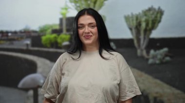 Şehir sokaklarında neşeli bir şekilde poz veren genç bir kadın. Açık hava yeşilliği ve gün boyunca şehir ortamında çekilen neşeli bir ifade..