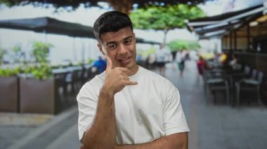 Genç adam canlı bir şehir caddesindeki terasta kafeler ve açık havada oturarak sıradan ve çekici bir şehir yaşam tarzını sergileyen bir telefon konuşması yapıyor..