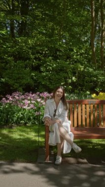 Hollanda, Lisse 'de bir lale bahçesinde bir bankta oturan bir kadın, canlı çiçekler ve yemyeşil ile çevrili, güneşli bir günün tadını çıkarıyor..