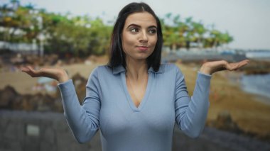 Mavi gömlekli kadın plajda kafa karışıklığı yaşıyor. Deniz manzarasının bulanık arka planı var..