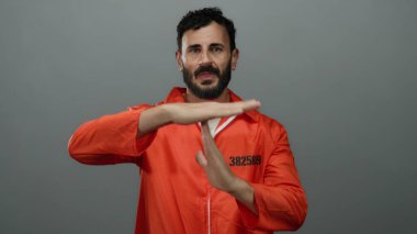 Turuncu tulumlu İspanyol bir adam gri arka planlı bir hapishane ortamında mola jesti yapıyor..