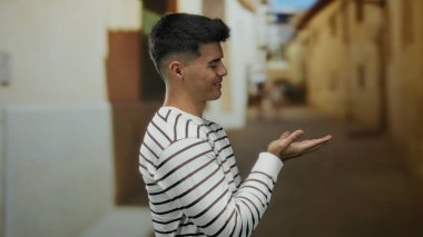 Çizgili tişörtlü genç adam elleri yana doğru uzanmış bir şekilde gülümsüyor şehir sokaklarında rahat ve mutlu bir şehir havası sergiliyor..