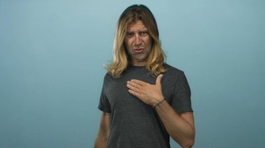 Stüdyoda eli göğsünde olan sarışın bir adam odaklanmış bakışlarını ve ince duruşunu gösteriyor..