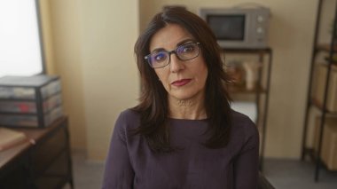 Orta yaşlı İspanyol kadın, ofis binasında parmağı olan siyah çerçeveli gözlükleri ayarlıyor..