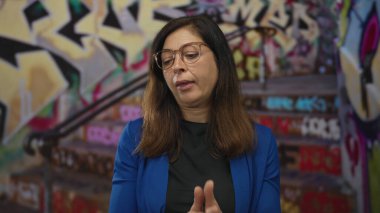 Kadın, renkli duvar resmi arkaplanının ortasında şehir grafiti caddesinde avuçlarını kaldırarak omuz silkiyor; belirsizlik.