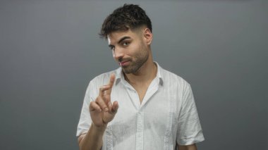 Stüdyoda, gri arka planı ve beyaz gömleği olan, yüzü odaklanmış, özgüveni olan genç İspanyol bir adam var..