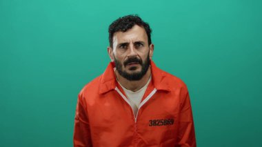 Turuncu hapishane tulumlu İspanyol bir adam yeşil arka planda ciddi ciddi kameraya bakıyor, ifadesiyle kasvetli ve düşünceli bir ruh hali içinde..