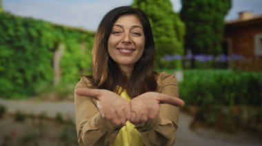 İspanyol orta yaşlı kadın, açık avuçlarını parlak güneş ışığı ve yemyeşil yaprakların altında tutuyor..