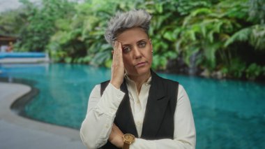 Beyaz gömlek ve siyah yelek giyen kadın, kapalı havuz güvertesinin yanındaki tapınakta dinleniyor..