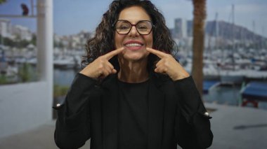 Limanda gülümseyen, arka planda tekneleri olan, gözlüklü ve dişlerini gösteren, güneşli bir günde, sakin bir deniz kenarında,.