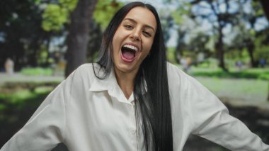 Parkta uzun siyah saçlı, beyaz tişört giyen, açık havada keyif ve tefekkür anı yakalayan bir kadın..