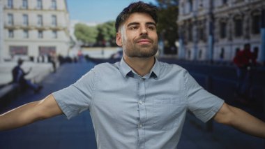 Gündüz vakti çıplak kolları havada ve gözleri kapalı bir adam işlek bir sokakta açık mavi gömlekli, dingin..