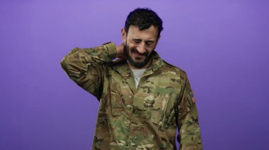 Askeri üniformalı İspanyol bir adam. Mor arka planda duran sakallı. Boynuna dokunarak rahatsızlığını gösteriyor..